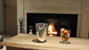A wooden table with a glass pitcher and a glass with oranges in front of a fireplace.