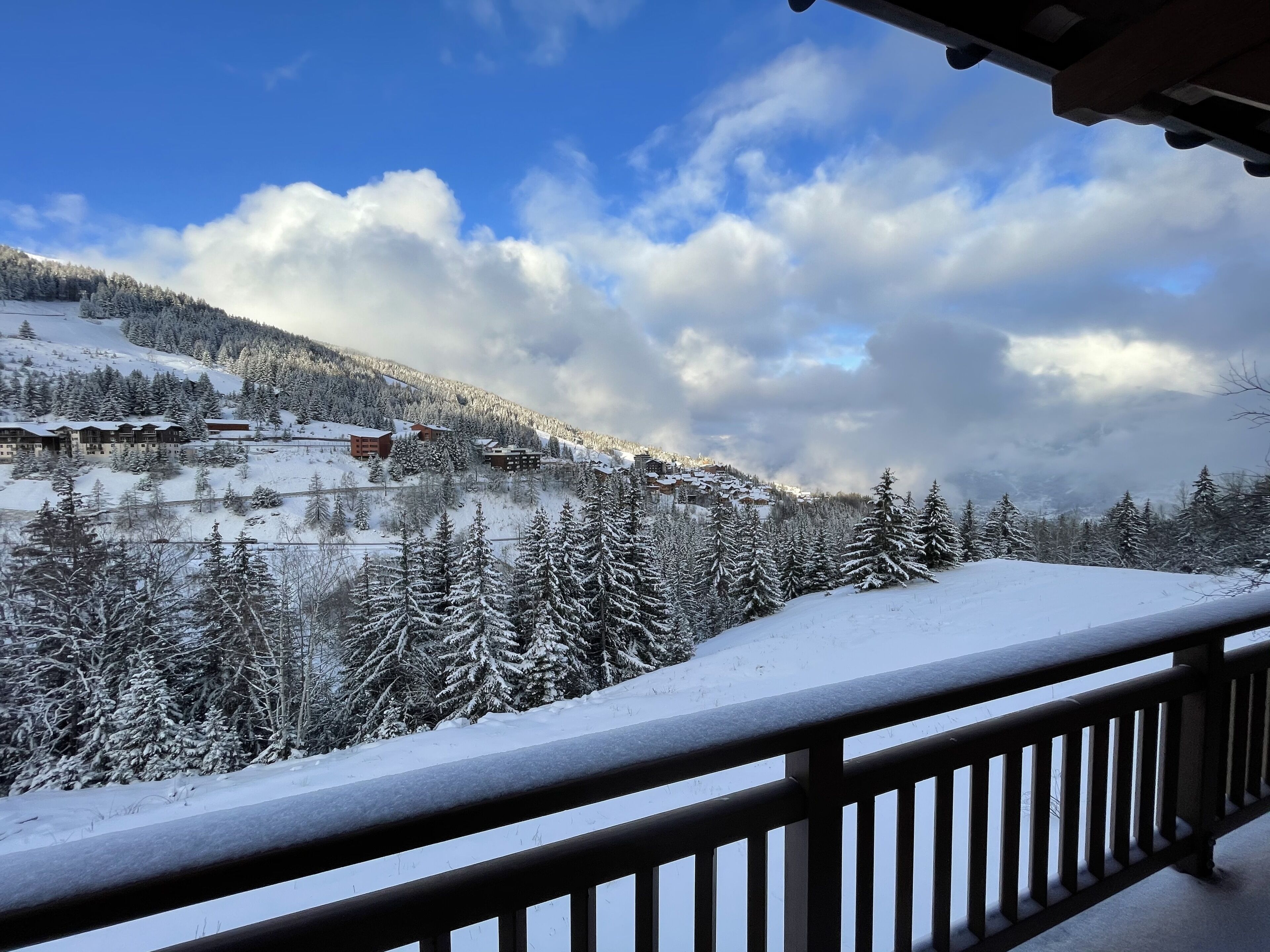 A snow-covered mountain landscape with a view of a resort area, including buildings and trees.