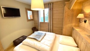 A bedroom with a bed, a television, a window with curtains, and a wooden headboard.