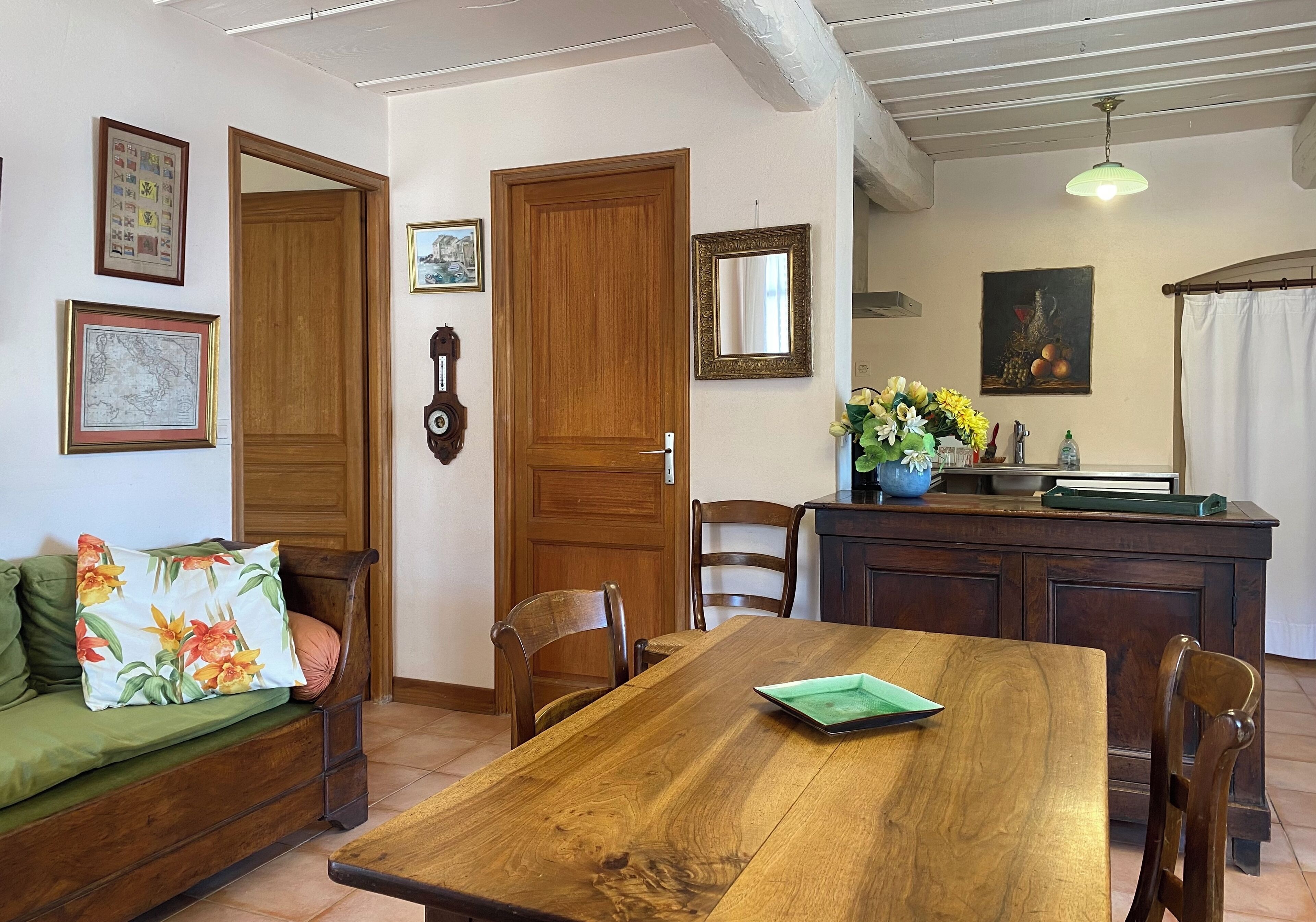 A dining area with a wooden table, chairs, a sofa, and a kitchen area with a sink and counter.