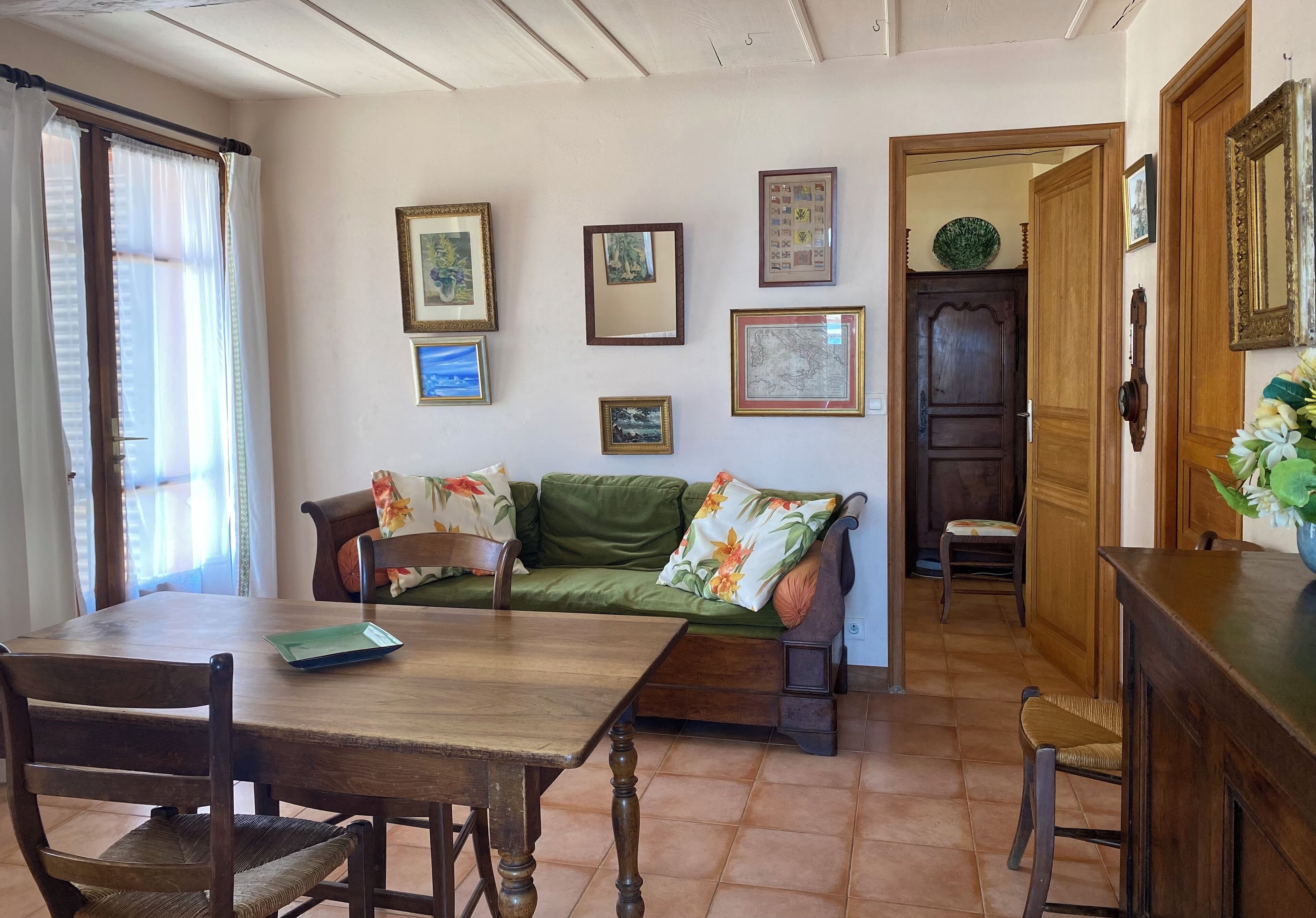A dining area with a wooden table and chairs, a green sofa with floral cushions, and a wall adorned with framed pictures.