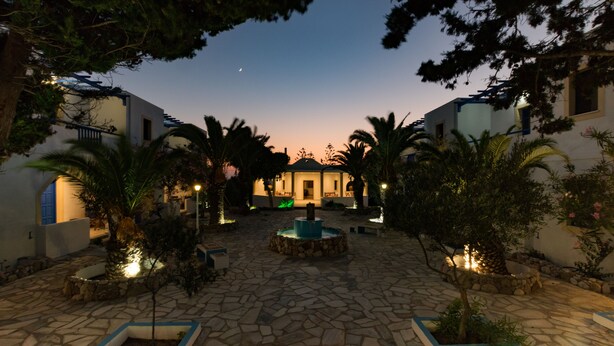A courtyard with stone flooring, palm trees, and a central fountain. - Summer Breeze (Karpathos)