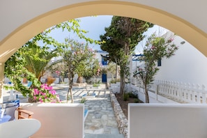 An outdoor courtyard with a stone pathway, white walls, and a white picket fence. - Summer Breeze (Karpathos)