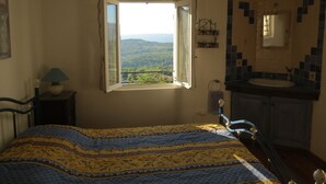 Un dormitori amb un llit, una finestra que ofereix vistes, una taula de nit amb una làmpada i un bany amb un lavabo i un mirall.