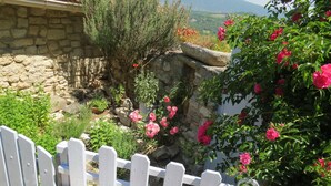 Mur de pedra amb una tanca de palets blancs i un jardí ple de flors roses.