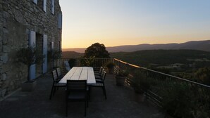 Edifici de pedra rústic amb una taula i caires de fusta preparats per dinar, amb vista a una vall pintoresca.