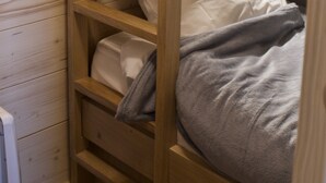 Una cama litera con escalera de madera, ropa de cama blanca y una manta gris.
