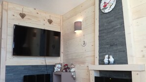 Una habitación acogedora con chimenea, televisor montado en la pared y repisas con adornos.
