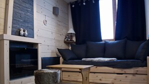 Una sala de estar acogedora con chimenea, un sofá, una mesita y un taburete mullido.