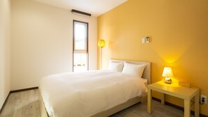 A bedroom with a bed, bedside table, lamp, and a window. - Painushima Resort (Ishigaki)