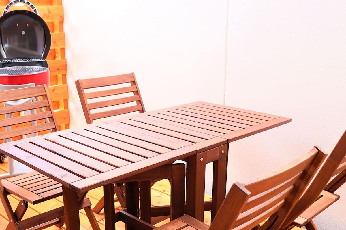 A wooden table and chairs set against a white wall with a wooden slat backdrop.
