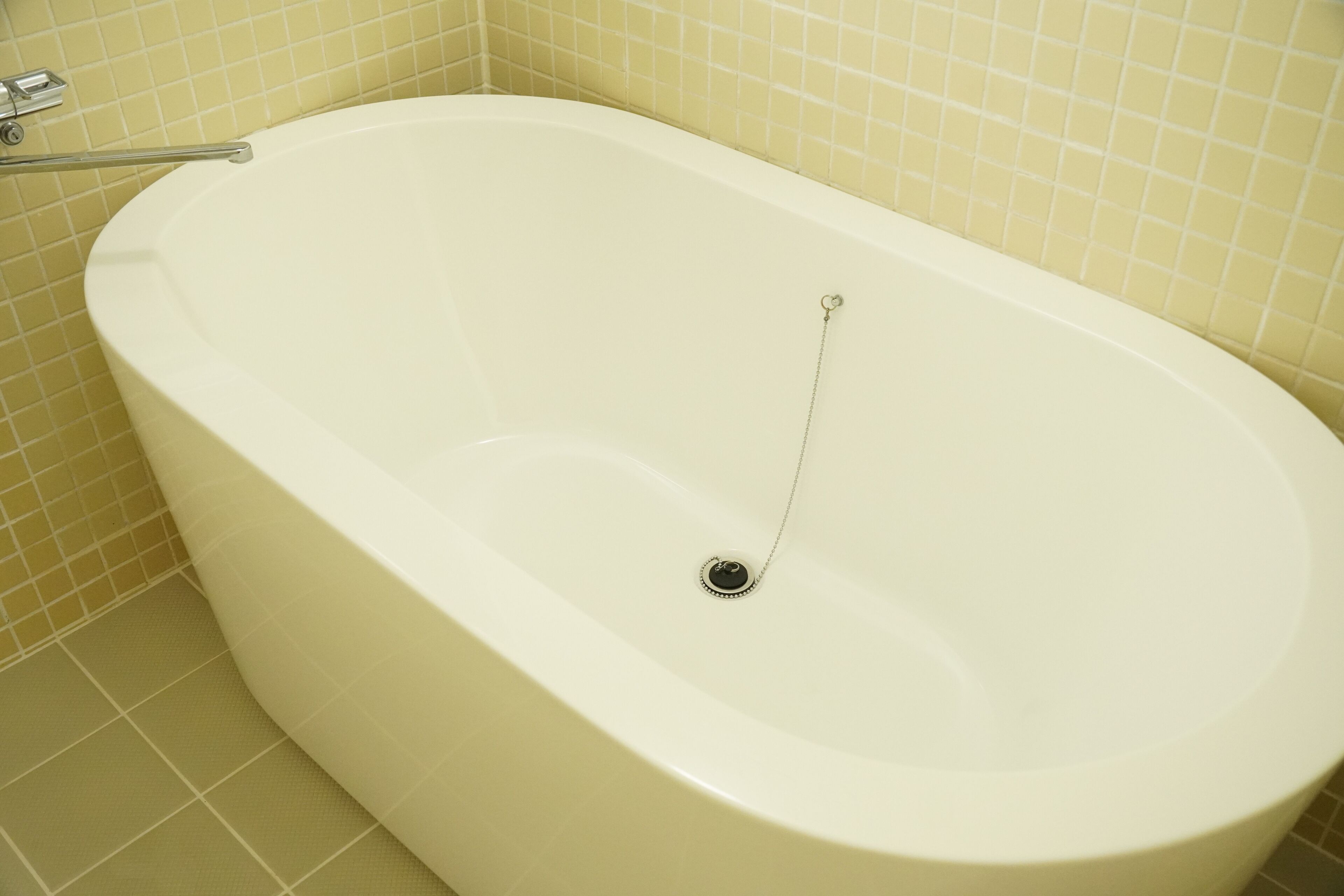 A white bathtub with a drain stopper and a metal grab bar.