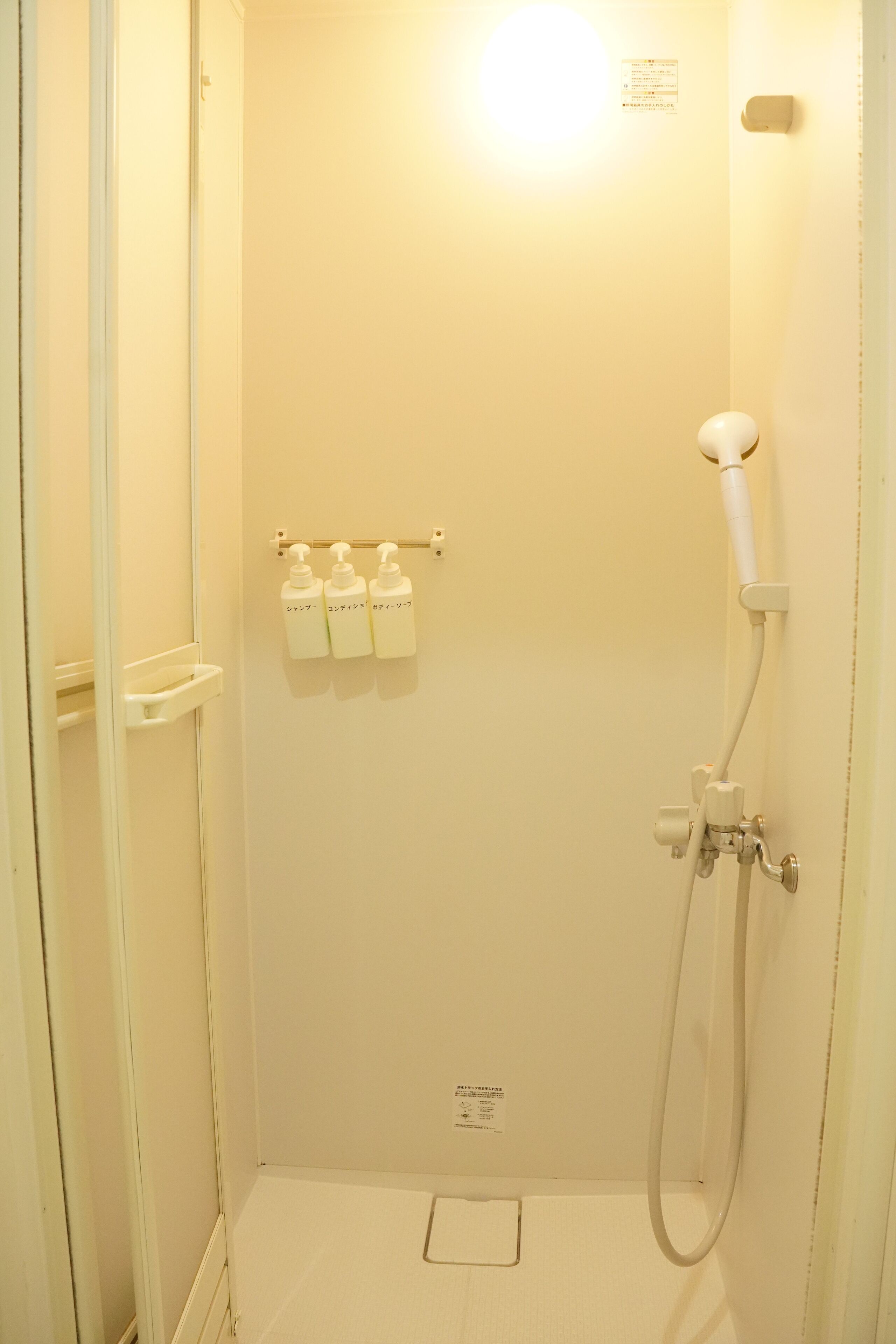 Un espacio de ducha pequeño y cerrado, con un cabezal de ducha manual, un dispensador de jabón en la pared y un perchero para toallas.