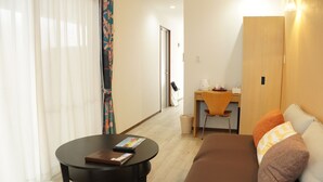 A modern room with a brown sofa, a round black table, and a wooden desk with a chair. - Painushima Resort (Ishigaki)