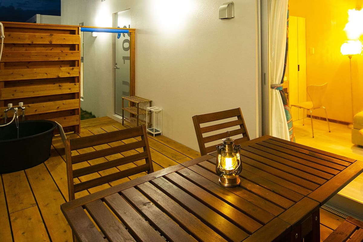 A wooden dining table with chairs, a lantern, and a view of a yellow-lit room with a sofa and a chair.