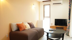A modern living room with a brown sofa, a round black coffee table, a flat-screen TV, and a window with curtains. - Painushima Resort (Ishigaki)