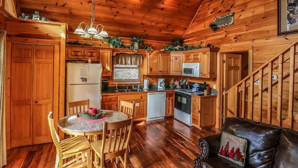 Interior de una cabaña de madera con cocina, comedor y una escalera.