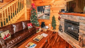 Un acogedor interior de cabaña con una escalera de madera, chimenea, sofá de cuero y un árbol de Navidad.