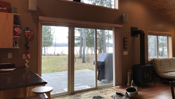 A cozy cabin interior with a large sliding glass door leading to a deck, a fireplace, and a high ceiling. - Lakeside bliss and serenity in the Northwoods (Makinen)