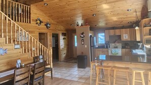 A wooden cabin interior with a dining area, kitchen, and a staircase leading to a loft. - Lakeside bliss and serenity in the Northwoods (Makinen)