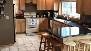 A kitchen with wooden cabinets, a stove, a sink, and bar stools. - Lakeside bliss and serenity in the Northwoods (Makinen)