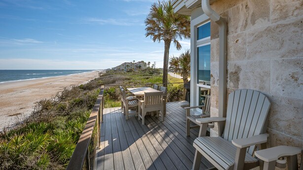 Een houten terras met tuinmeubilair met uitzicht op een strand.