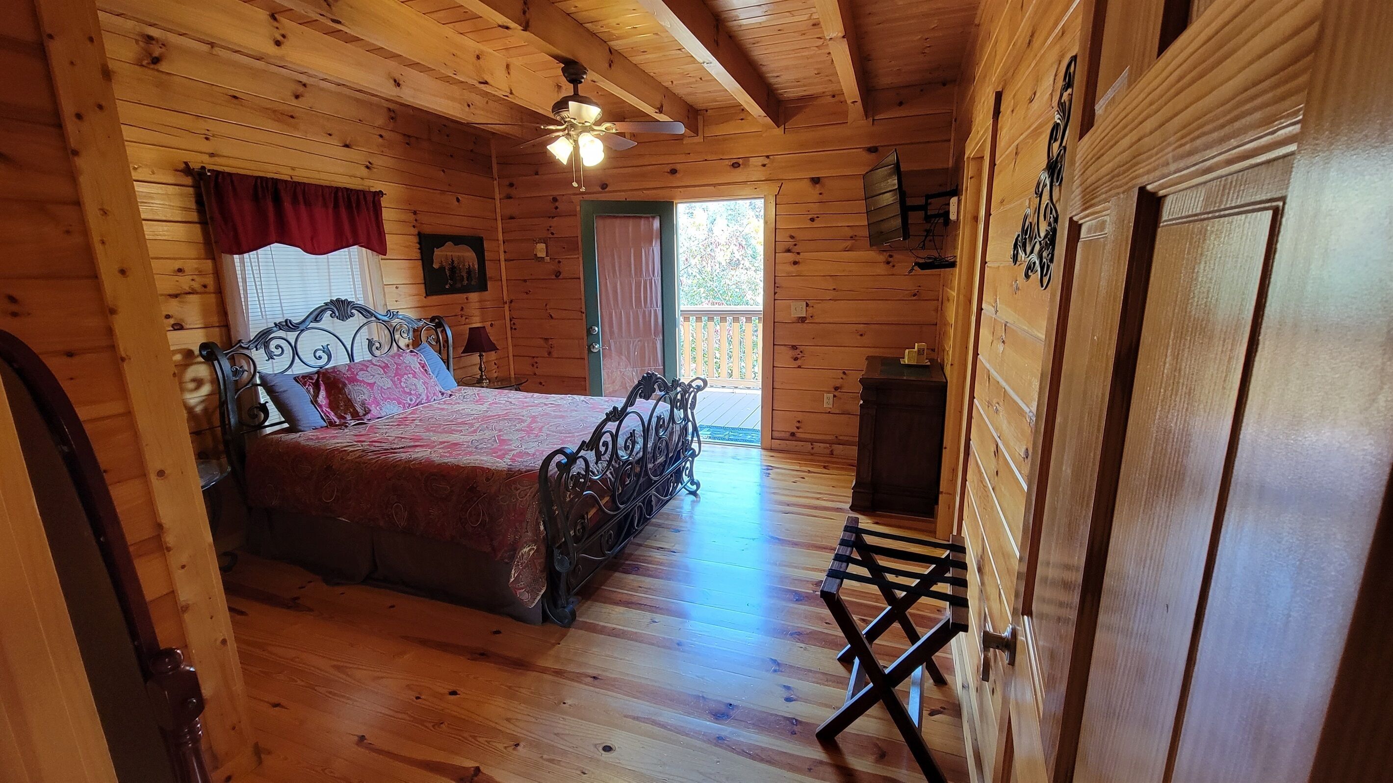 Een houten slaapkamer met een bed, een plafondventilator, een raam en een deur.