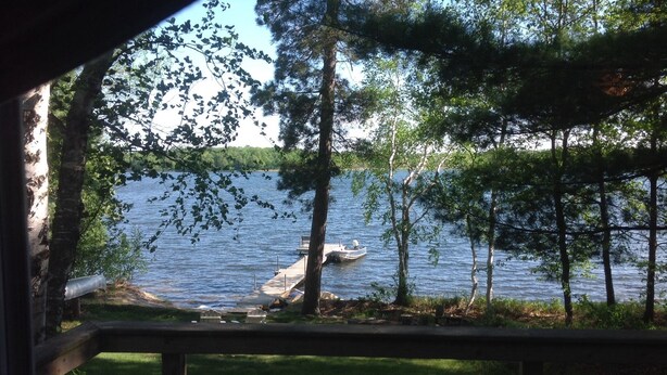 A lakeside view from a covered deck with a dock and boat. - Quiet, Cozy Lake Cottage North of Merrifield, Great Getaway! (Merrifield)