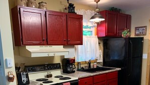 A kitchen with red cabinets, a black refrigerator, a stove, and a coffee maker. - Quiet, Cozy Lake Cottage North of Merrifield, Great Getaway! (Merrifield)