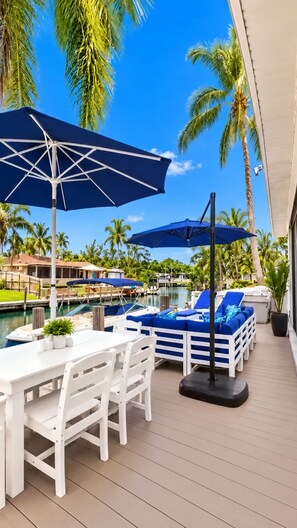 A deck with white furniture, blue umbrellas, and a pool area with lounge chairs.