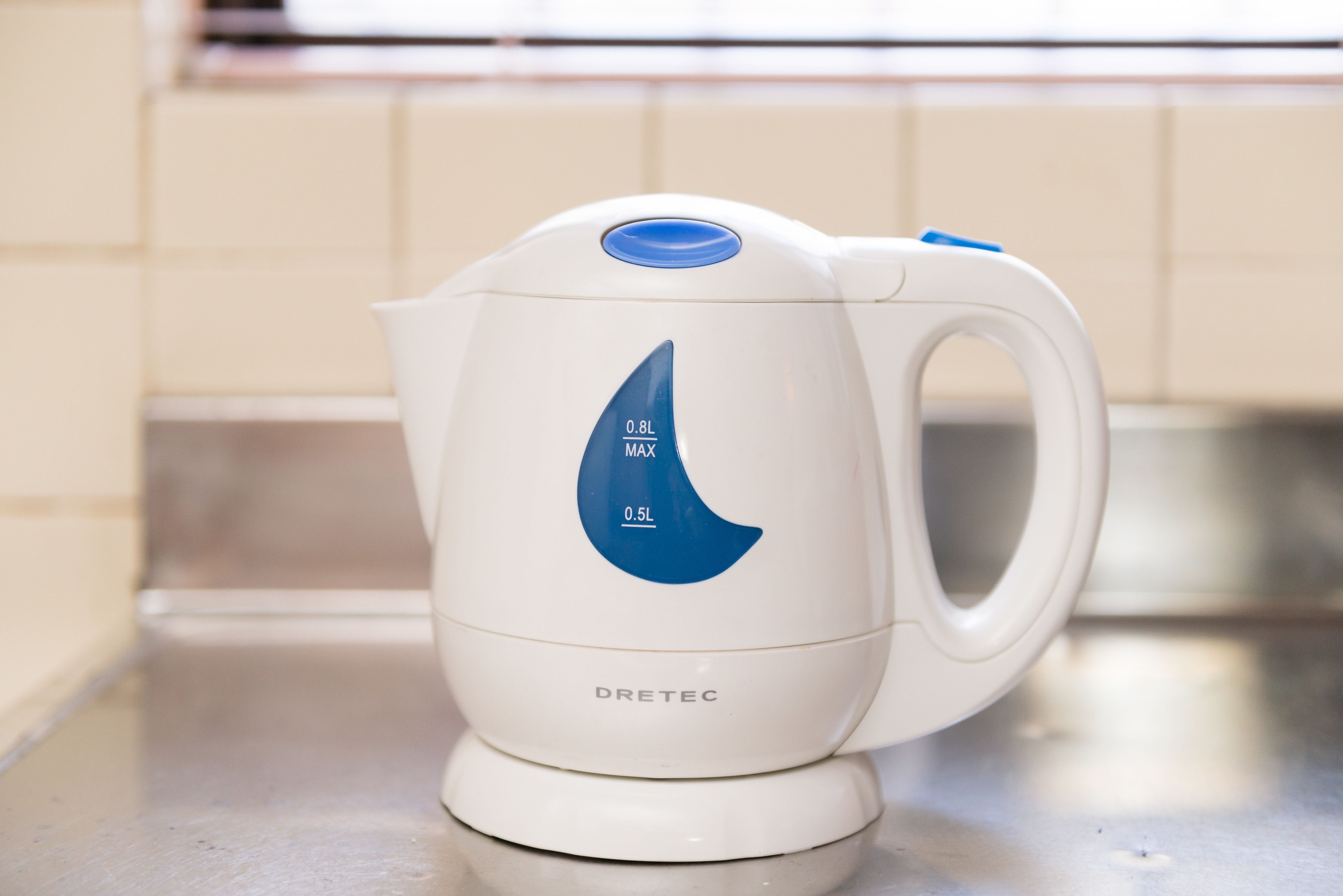 A white electric kettle with a blue control panel and a handle, placed on a kitchen countertop.