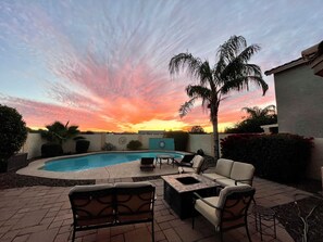 A pool area with lounge chairs and a palm tree, surrounded by a low wall and various plants. - Private Heated Pool, Cozy Heated Patio & Spectacular AZ Sunsets! (Queen Creek)