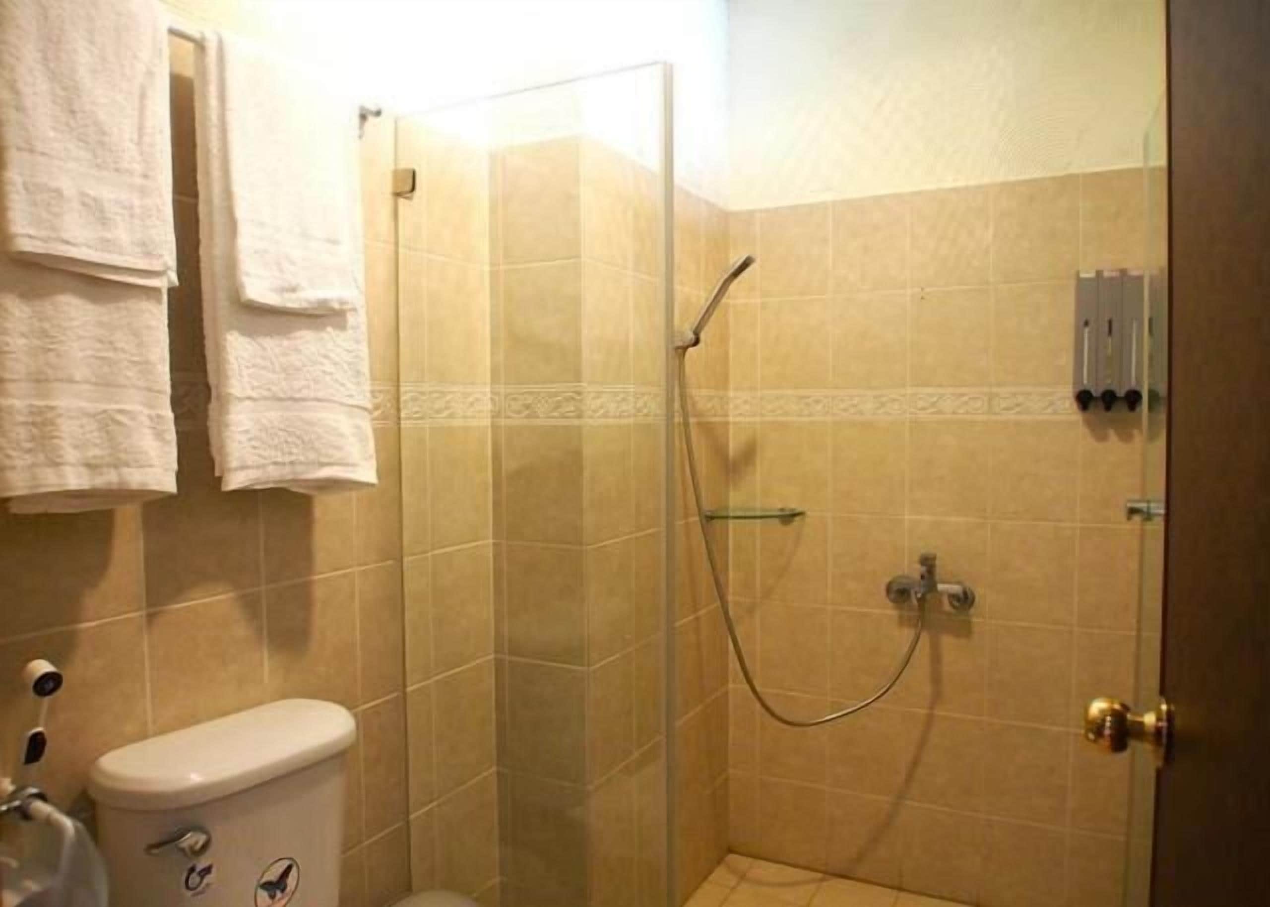 A bathroom with a toilet, a shower with a glass door, and a towel rack with towels.