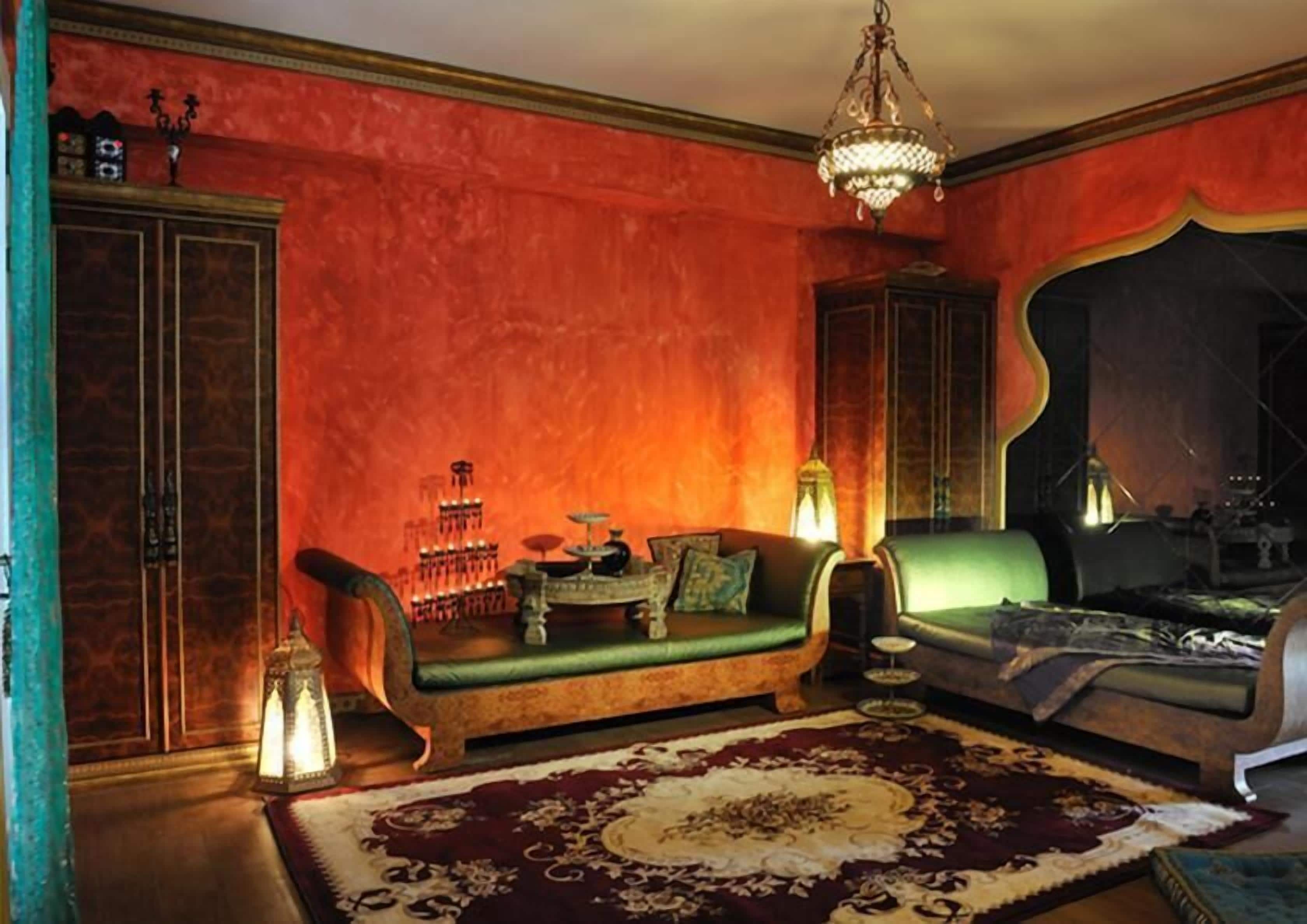 A room with a red-walled interior, a green sofa, a patterned rug, and a chandelier.