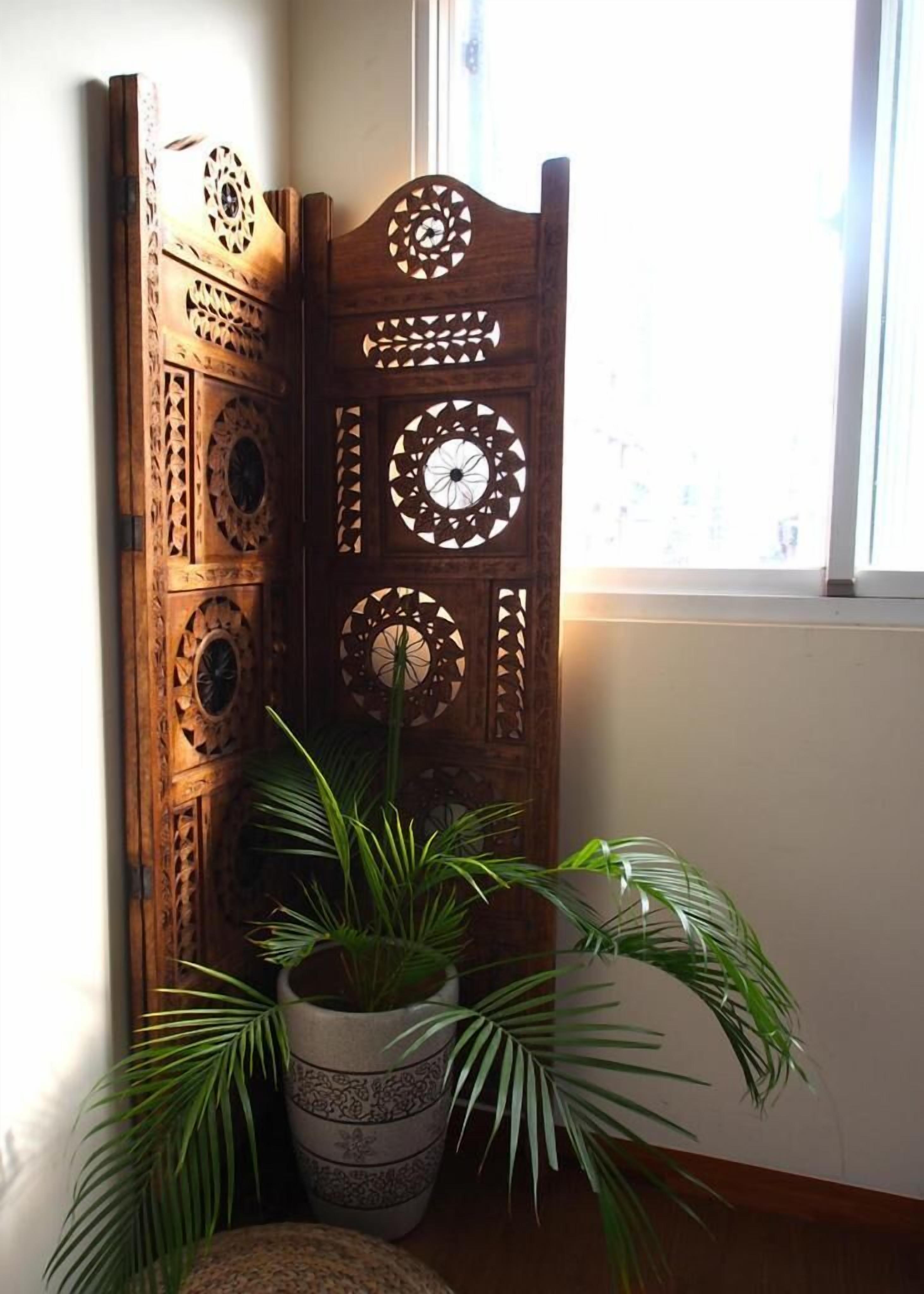 A wooden partition with intricate cut-out designs, a potted plant, and a window with natural light.