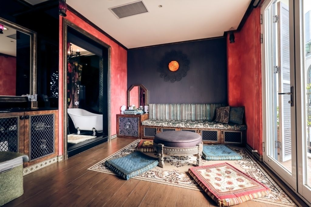 A room with a wooden floor, a bench with cushions, a large mirror, and a round wall decoration.