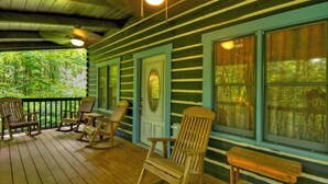 A wooden porch with rocking chairs and a bench, overlooking a forested area. - Sans Souci | Pet Friendly (Copperhill)