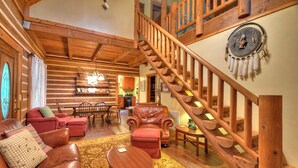 A log cabin interior with a wooden staircase, leather furniture, and a dining area. - Sans Souci | Pet Friendly (Copperhill)