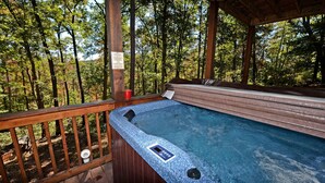 Ein Whirlpool mit Holzterrasse und Wald im Hintergrund.