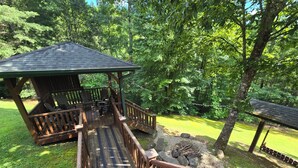 A wooden deck with Adirondack chairs and a gazebo, surrounded by lush greenery. - 4 bd cabin with gorgeous sunset view and minutes to everything.  (Gatlinburg)