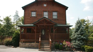 A two-story wooden building with a porch, stone foundation, and a small garden with flowers. - 4 bd cabin with gorgeous sunset view and minutes to everything.  (Gatlinburg)