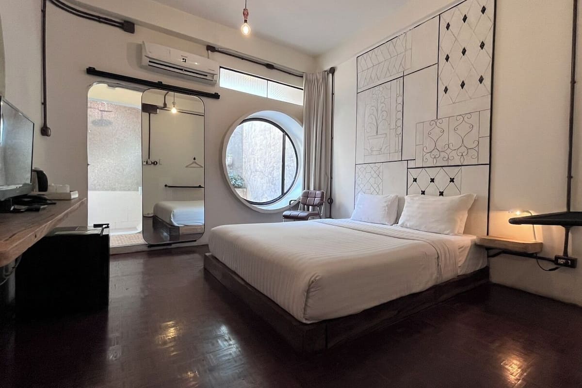 Une chambre d’hôtel moderne dotée d’un grand lit, d’un bureau avec un ordinateur, d’une fenêtre ronde et d’un téléviseur fixé au mur.
