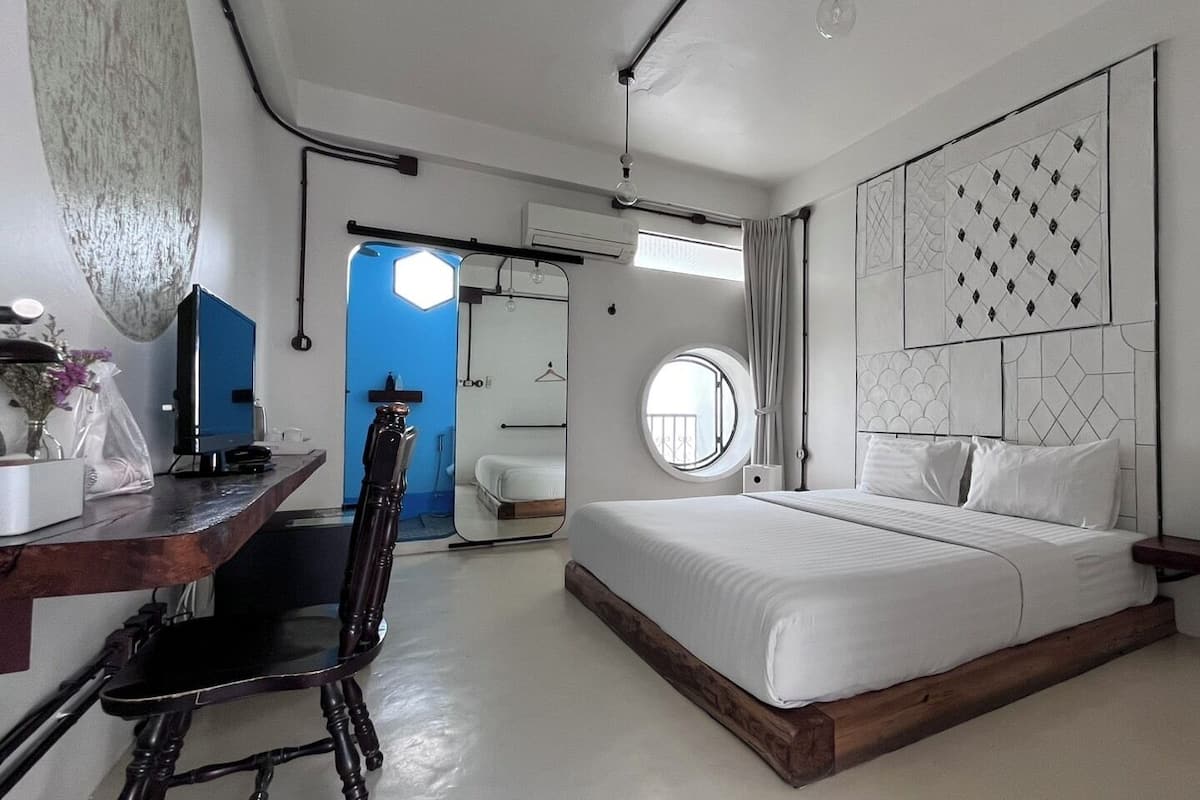 Une chambre d’hôtel moderne avec un grand lit, un bureau avec une chaise, un miroir et une armoire.