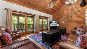 A log cabin interior with a large window, a television, a black entertainment unit, and a patterned rug. - The Red Elk Lodge! Lakefront in Quiet Cove with Private Dock and Fishing Canoes! (Branson)