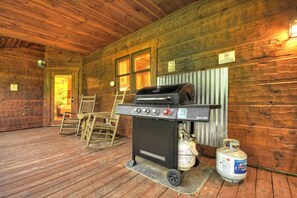 A wooden cabin with a grill and propane tank on the porch.