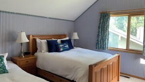 Ein Schlafzimmer mit einem hölzernen Bett, zwei Nachttischen, einem Fenster mit Vorhängen und rauen Tapeten.