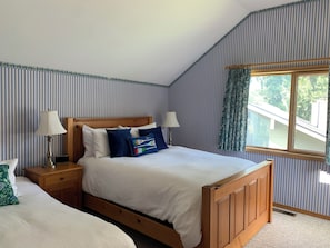 A bedroom with a wooden bed, two bedside tables, a window with curtains, and striped wallpaper.