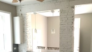 Un baño con pared de ladrillo blanco, ventilador de techo, espejo grande y ventana.