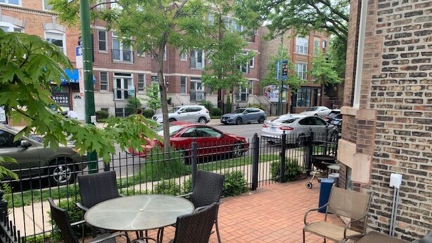Un patio con mobiliario exterior y vistas a coches aparcados y edificios al fondo.