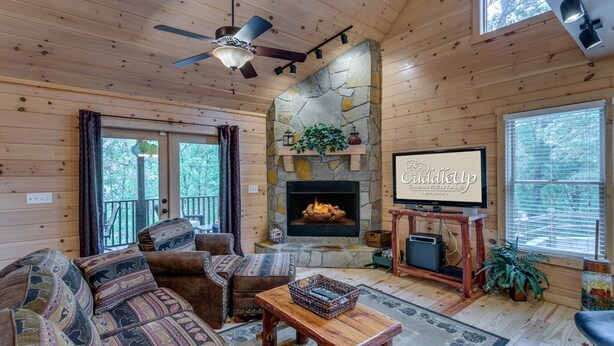 A cozy cabin interior with a stone fireplace, a ceiling fan, and a television on a wooden stand. - Country Dreams | Near Ocoee River | Hot Tub | Fire Pit (Copperhill)